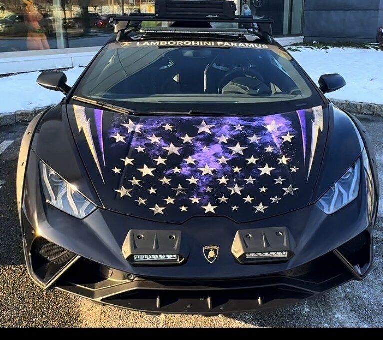 Black Lamborghini Huracán Sterrato in Outrun Opioids livery, seen head-on with a purple star-spangled hood wrap, roof-mounted light bar and a Lamborghini Paramus windshield banner