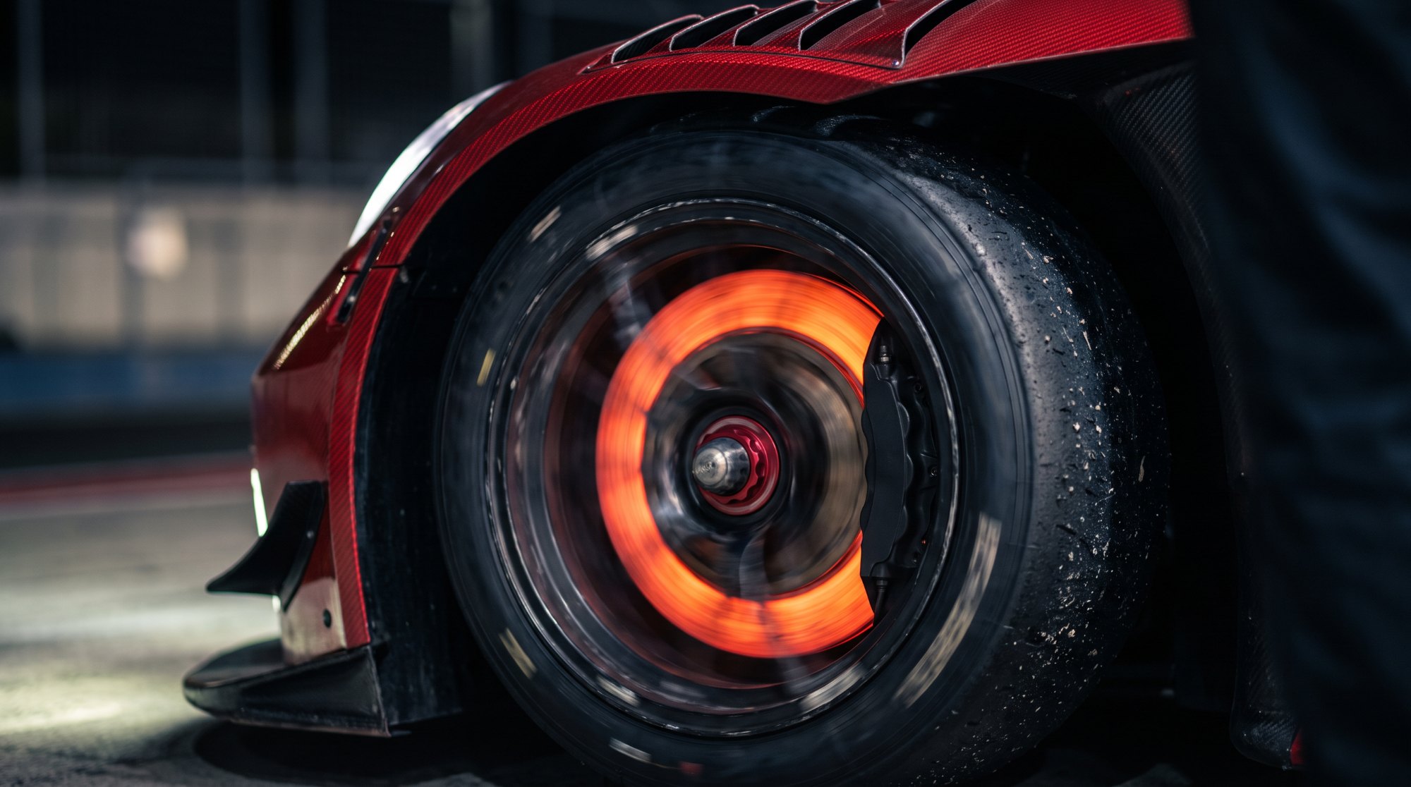 Glowing steel brake disc and black caliper behind a racing wheel with a slick tyre
