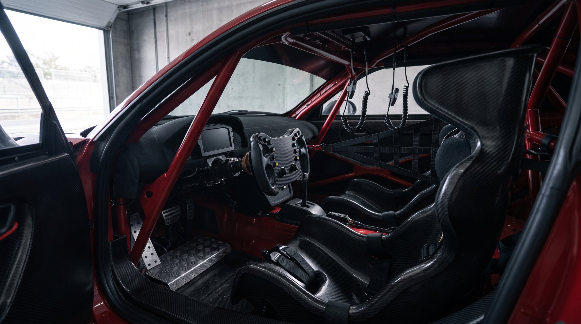 Two-seat GT race car cockpit with carbon bucket seats, harnesses and a roll cage