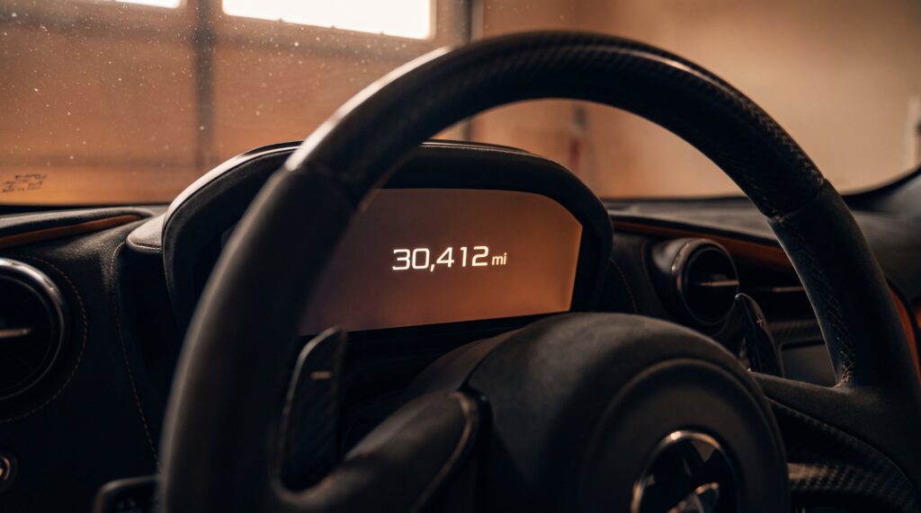 Exotic car mileage shown on a supercar digital instrument cluster reading 30,412 miles, seen through the steering wheel in a dim garage