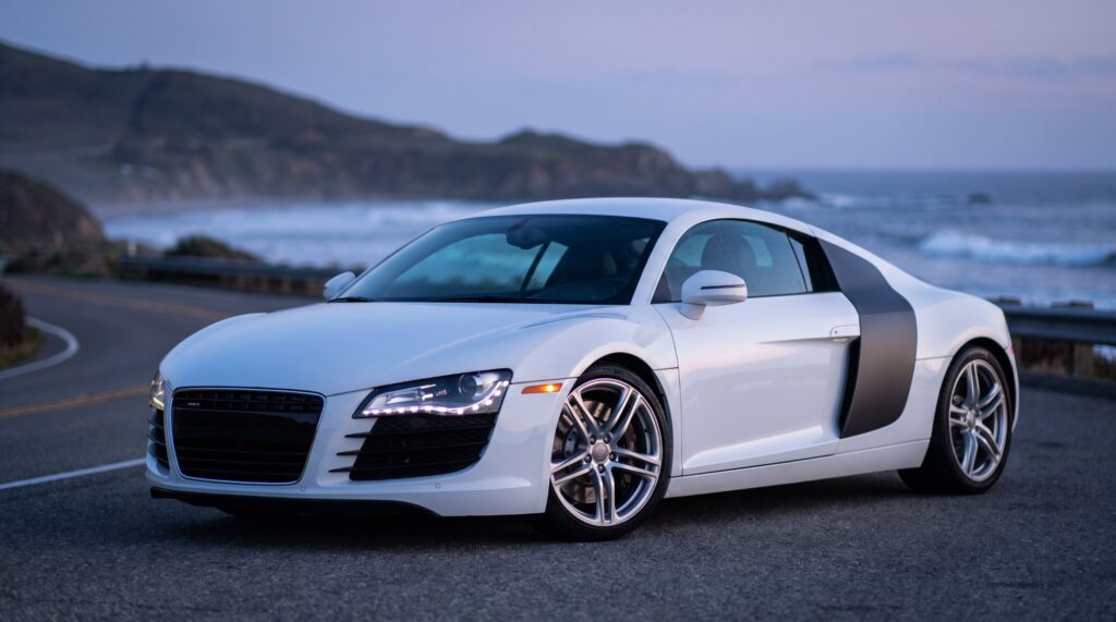 White first-generation Audi R8 coupe with dark side blades parked on a coastal road at dusk