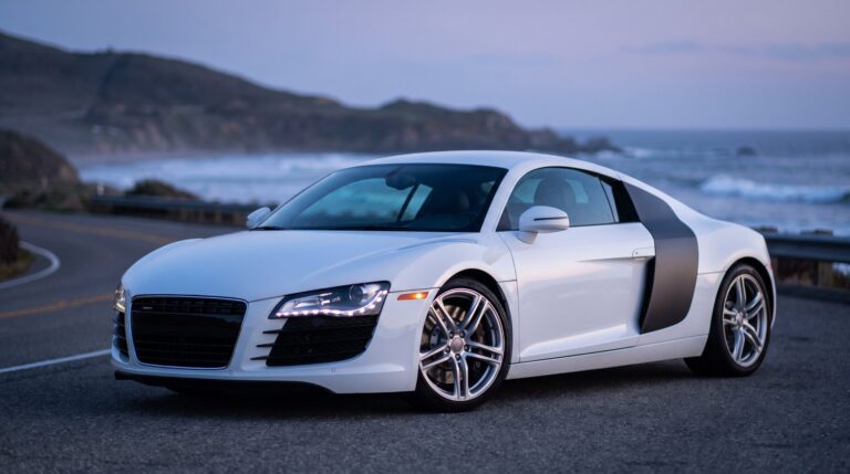 White first-generation Audi R8 coupe with dark side blades parked on a coastal road at dusk