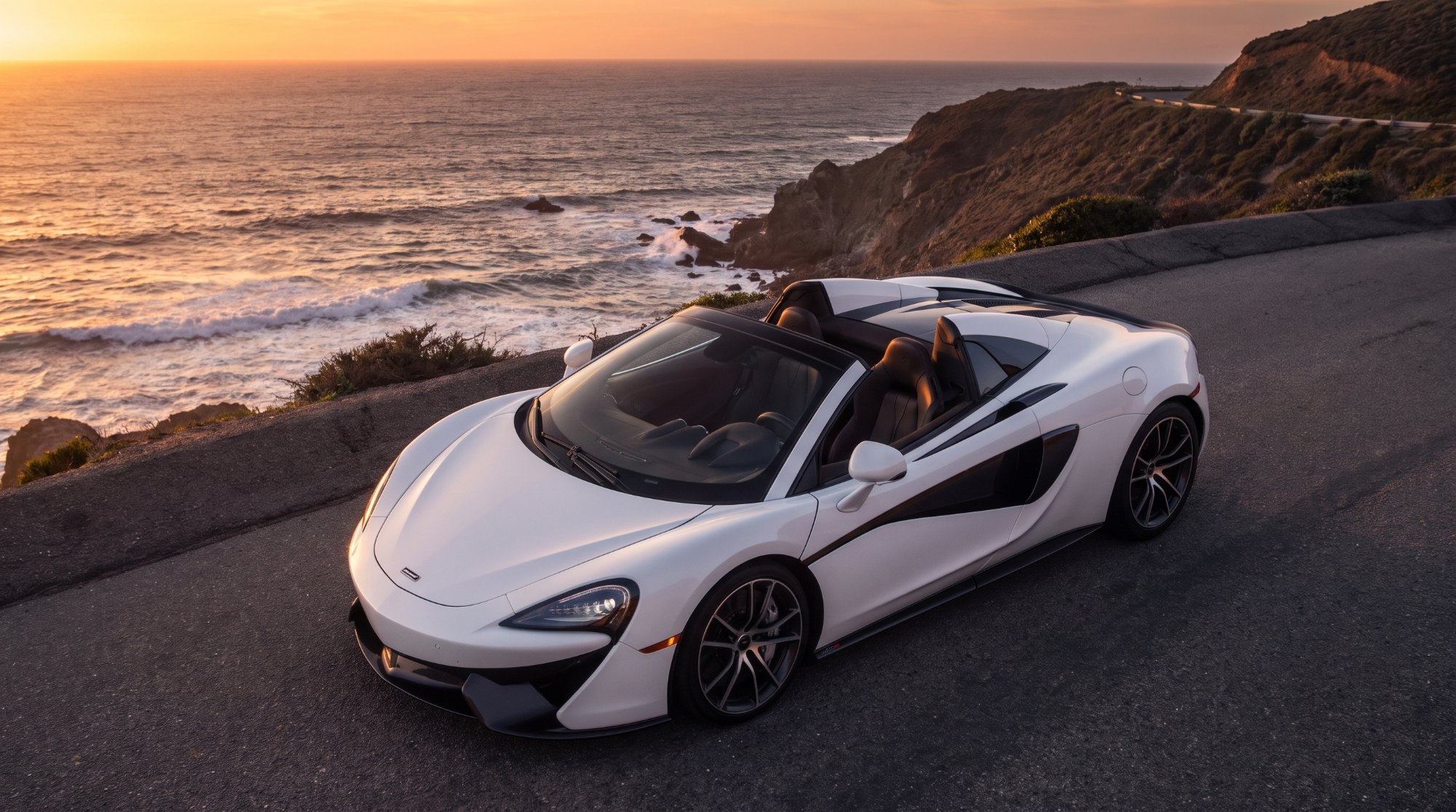 Used McLaren 570S Spider in white with its hardtop stowed, parked on a coastal overlook at sunset (AI-generated illustration)